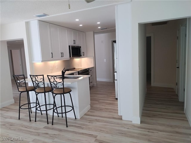 kitchen featuring sink, a kitchen breakfast bar, light hardwood / wood-style floors, a textured ceiling, and white cabinets