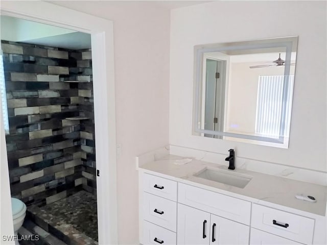 bathroom featuring ceiling fan, toilet, vanity, and tiled shower