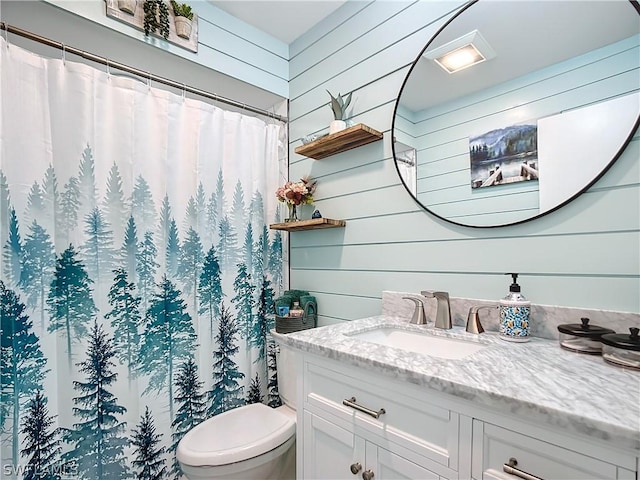 bathroom with toilet, vanity, and wooden walls