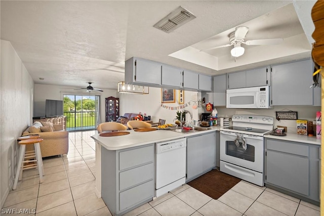 kitchen with white appliances, sink, a raised ceiling, kitchen peninsula, and light tile patterned flooring