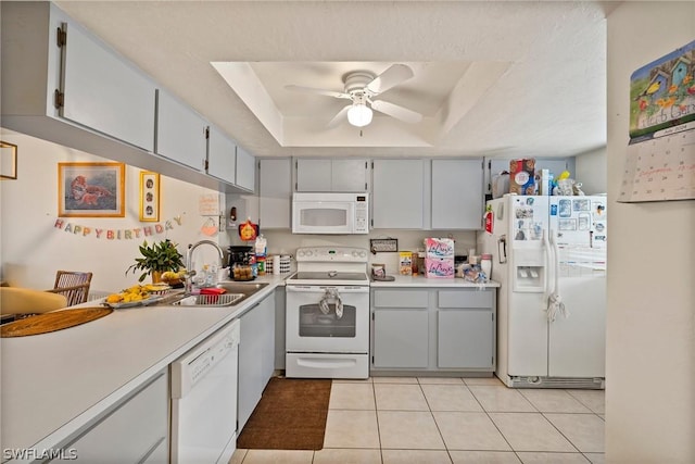 kitchen with white appliances, a tray ceiling, sink, ceiling fan, and light tile patterned floors