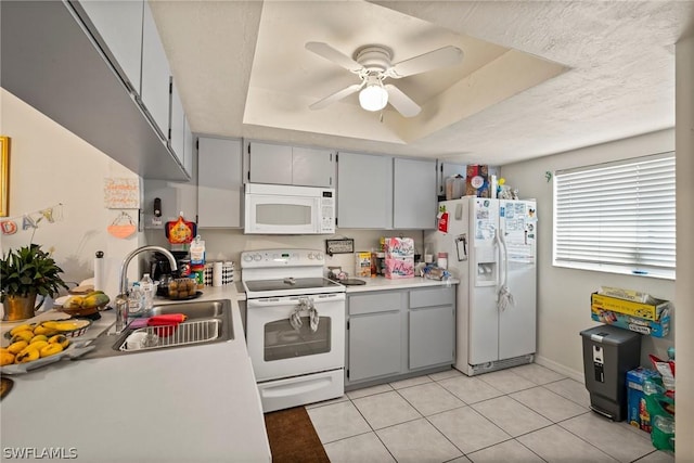 kitchen with white appliances, light tile patterned floors, gray cabinetry, sink, and a tray ceiling