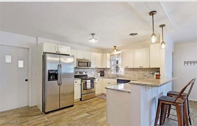 kitchen with kitchen peninsula, stainless steel appliances, light hardwood / wood-style floors, light stone countertops, and hanging light fixtures