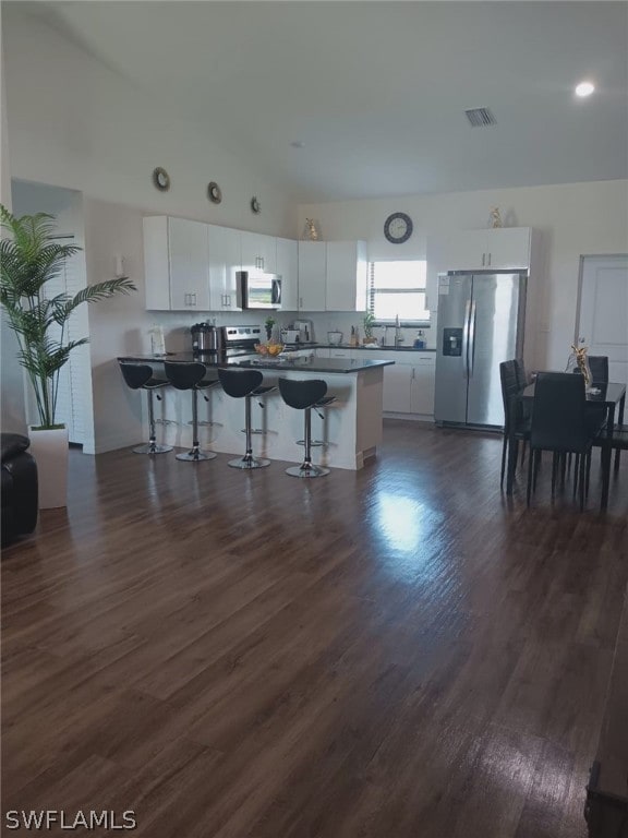 kitchen featuring white cabinetry, lofted ceiling, stainless steel appliances, dark hardwood / wood-style floors, and a kitchen bar