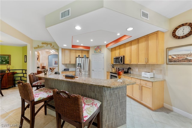 kitchen featuring appliances with stainless steel finishes, light brown cabinets, light tile patterned floors, decorative backsplash, and light stone countertops