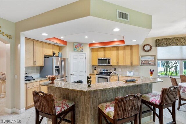 kitchen with light brown cabinets, light stone countertops, backsplash, and stainless steel appliances