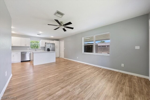 unfurnished living room with light wood-style floors, a ceiling fan, visible vents, and baseboards