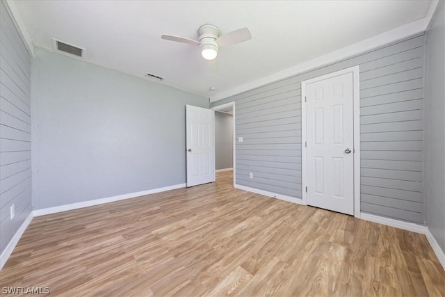 unfurnished bedroom with light wood-type flooring, visible vents, and wooden walls