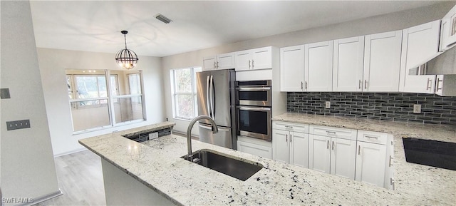 kitchen featuring light stone countertops, white cabinetry, stainless steel appliances, sink, and hanging light fixtures