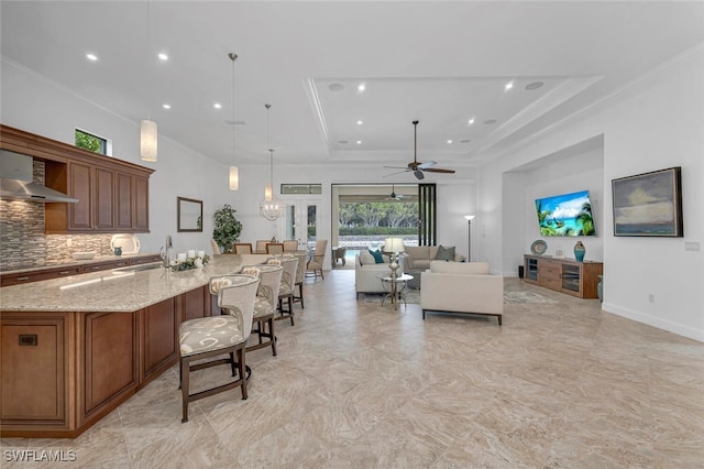 kitchen with light stone counters, a kitchen breakfast bar, decorative backsplash, a raised ceiling, and pendant lighting