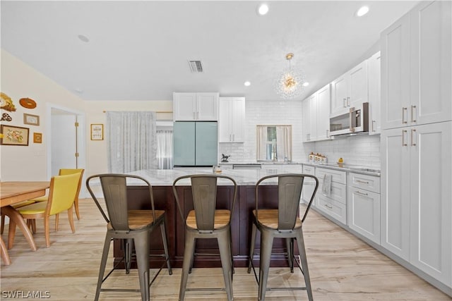 kitchen featuring appliances with stainless steel finishes, light stone countertops, a kitchen bar, a kitchen island, and white cabinetry