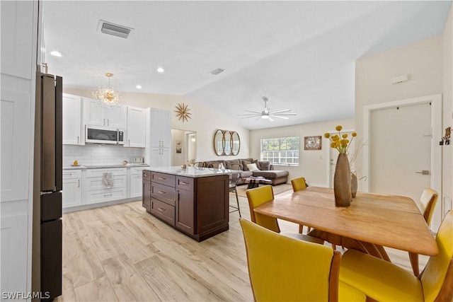 kitchen featuring stainless steel appliances, white cabinets, a center island, lofted ceiling, and tasteful backsplash