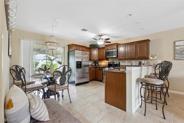 kitchen with appliances with stainless steel finishes, decorative light fixtures, kitchen peninsula, light tile patterned floors, and stone counters