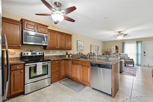 kitchen featuring kitchen peninsula, sink, appliances with stainless steel finishes, light tile patterned floors, and dark stone counters