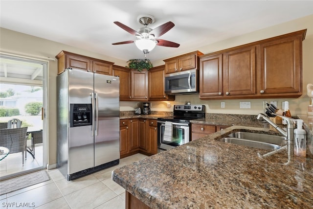 kitchen with stainless steel appliances, dark stone counters, sink, light tile patterned flooring, and ceiling fan