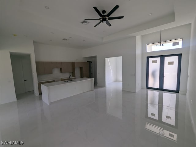 unfurnished living room with a tray ceiling, ceiling fan, light tile patterned floors, and sink