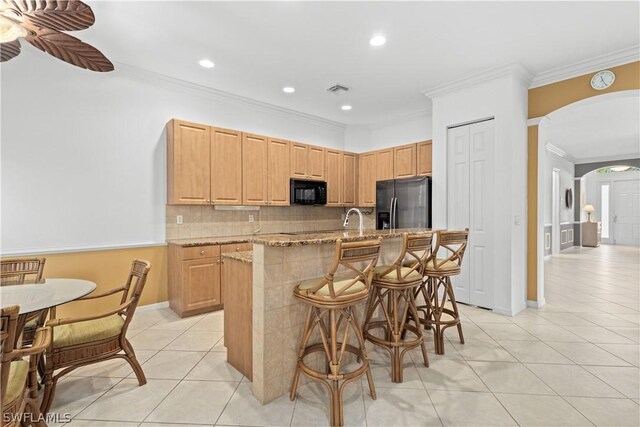 kitchen featuring light brown cabinetry, light stone counters, ceiling fan, stainless steel fridge with ice dispenser, and a breakfast bar