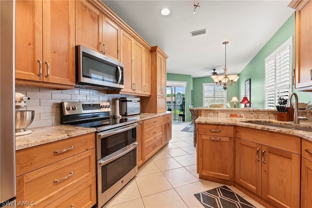 kitchen with light tile patterned floors, stainless steel appliances, light stone countertops, decorative backsplash, and sink