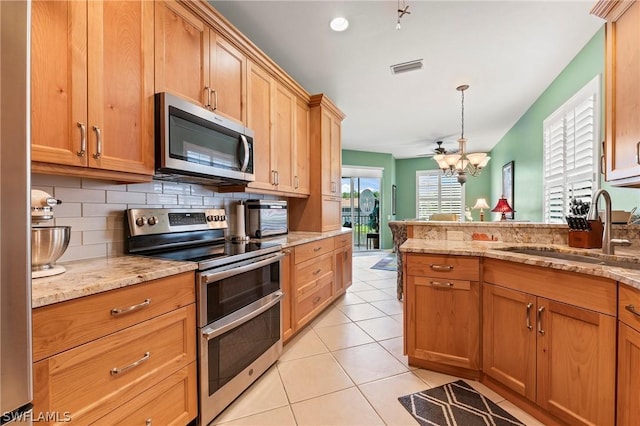 kitchen featuring sink, light tile patterned floors, appliances with stainless steel finishes, pendant lighting, and light stone countertops