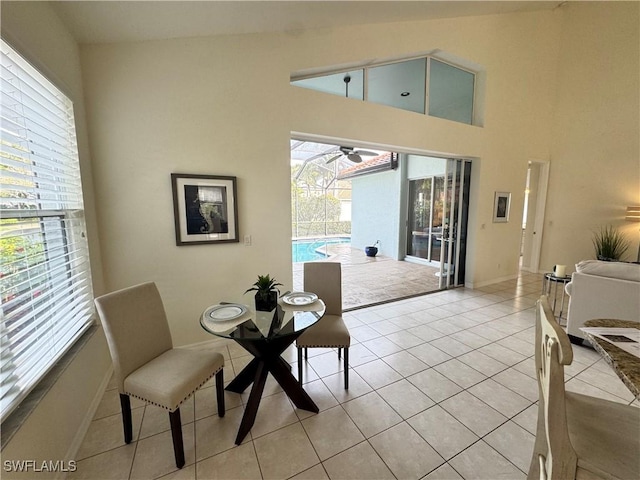 dining area with light tile patterned floors, baseboards, a ceiling fan, a sunroom, and high vaulted ceiling