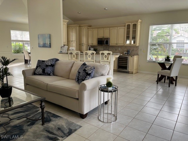 living room with wine cooler, lofted ceiling, baseboards, and light tile patterned floors