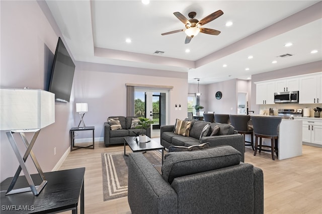 living room with a tray ceiling, ceiling fan, and light hardwood / wood-style flooring