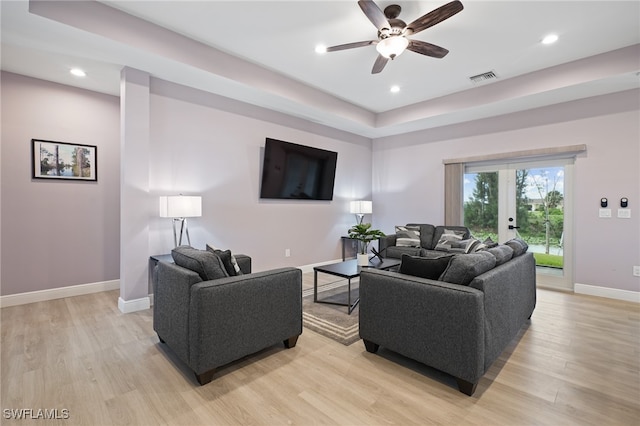 living room with french doors, light hardwood / wood-style floors, a raised ceiling, and ceiling fan