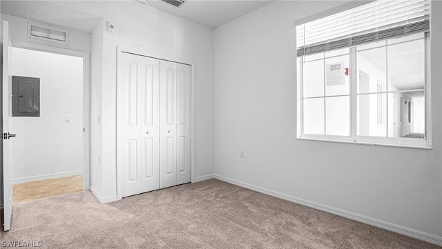 unfurnished bedroom featuring multiple windows, light colored carpet, electric panel, and a closet