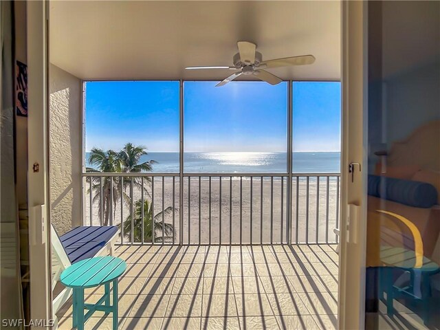 sunroom / solarium with ceiling fan, a water view, a beach view, and plenty of natural light