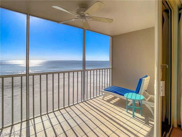 unfurnished sunroom with ceiling fan, a water view, a healthy amount of sunlight, and a beach view