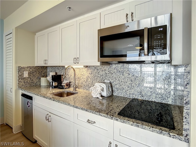 kitchen with white cabinetry, sink, light stone countertops, stainless steel appliances, and backsplash