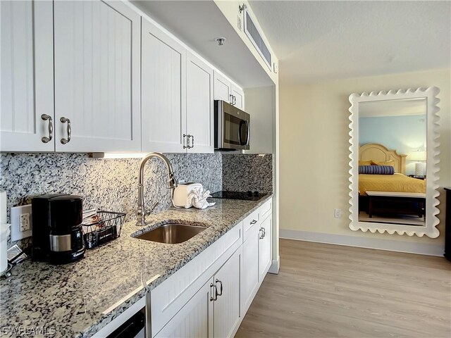 kitchen with sink, light hardwood / wood-style flooring, decorative backsplash, light stone countertops, and white cabinetry