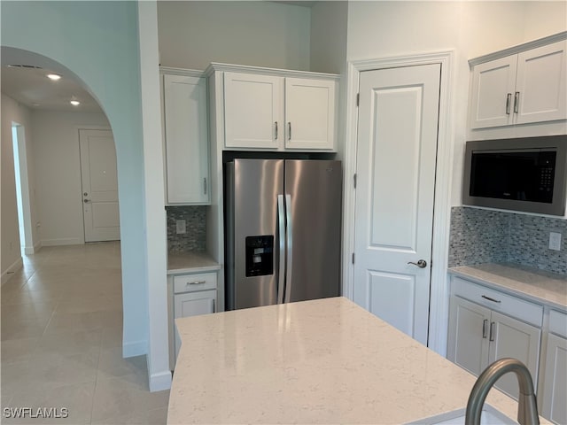 kitchen with white cabinets, backsplash, light stone counters, and stainless steel appliances