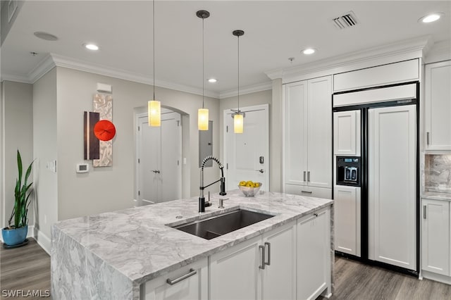 kitchen featuring sink, light stone counters, an island with sink, paneled fridge, and white cabinets