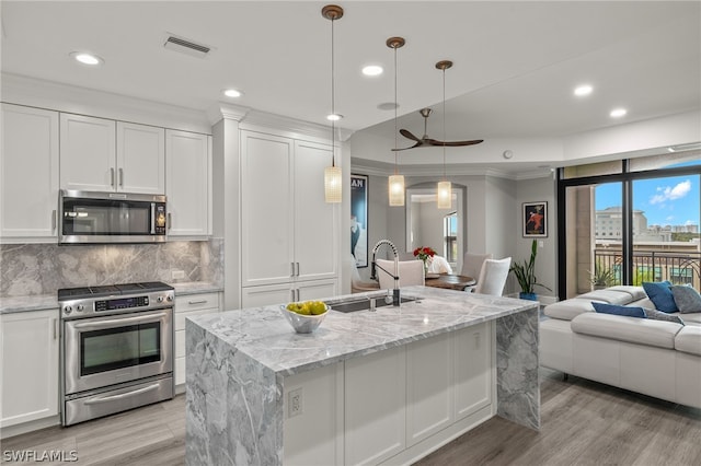 kitchen with decorative light fixtures, sink, white cabinets, stainless steel appliances, and a center island with sink