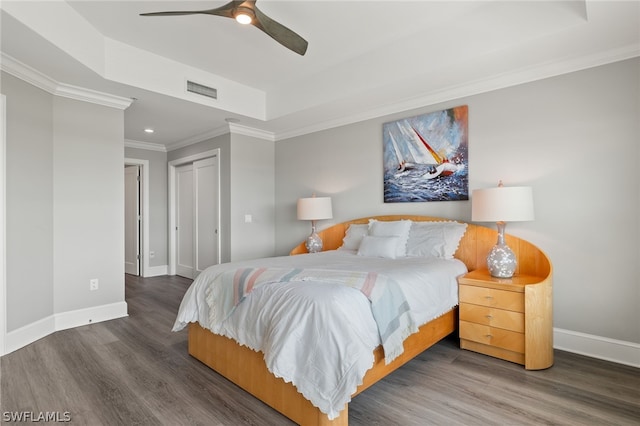 bedroom featuring dark wood-type flooring, ceiling fan, ornamental molding, a raised ceiling, and a closet