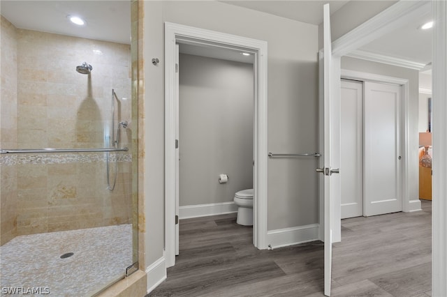 bathroom with hardwood / wood-style floors, crown molding, toilet, and tiled shower