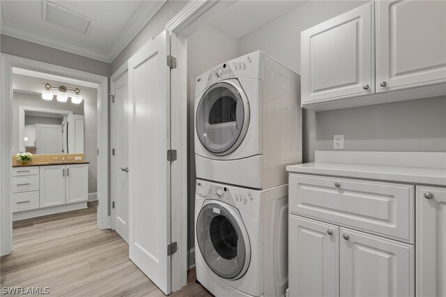 laundry room featuring stacked washer and dryer, ornamental molding, sink, and light wood-type flooring