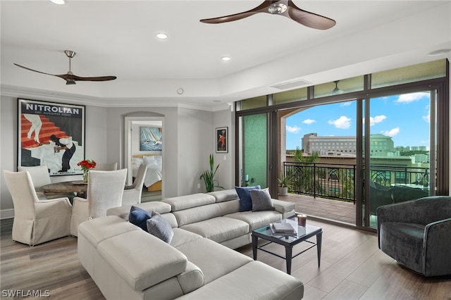 living room featuring a raised ceiling, ceiling fan, crown molding, and light hardwood / wood-style floors