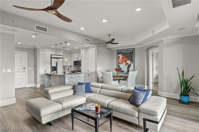 living room featuring sink, a tray ceiling, light hardwood / wood-style floors, and ceiling fan