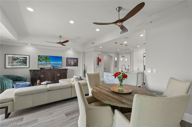 dining room featuring ceiling fan, a tray ceiling, sink, and light wood-type flooring