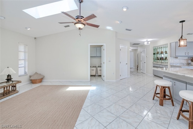 living room with vaulted ceiling with skylight, light tile patterned floors, and ceiling fan