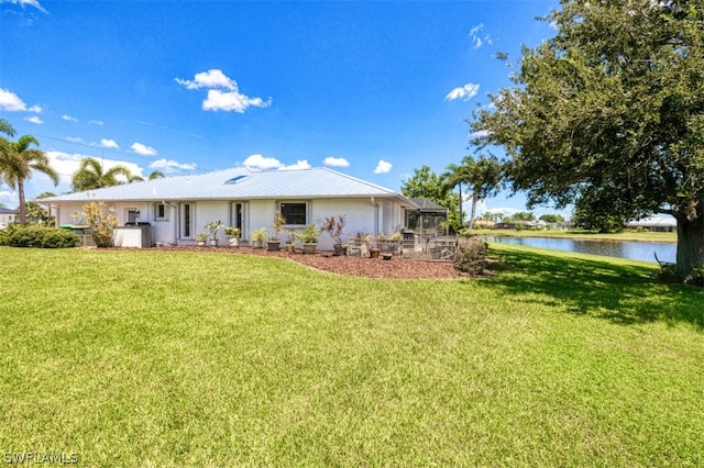 back of property with a water view, a lanai, and a lawn