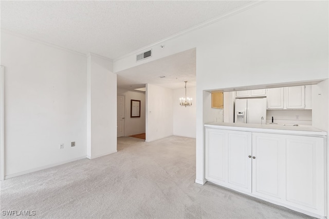 empty room featuring light colored carpet, a textured ceiling, and a notable chandelier