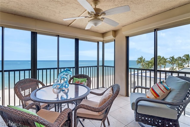 sunroom featuring a water view, ceiling fan, and a view of the beach