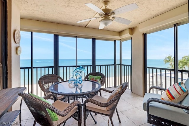 sunroom / solarium with a water view, ceiling fan, and a view of the beach