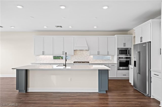 kitchen featuring white cabinetry, custom exhaust hood, appliances with stainless steel finishes, a kitchen island with sink, and sink