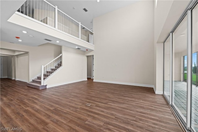 unfurnished living room featuring a high ceiling and dark hardwood / wood-style floors