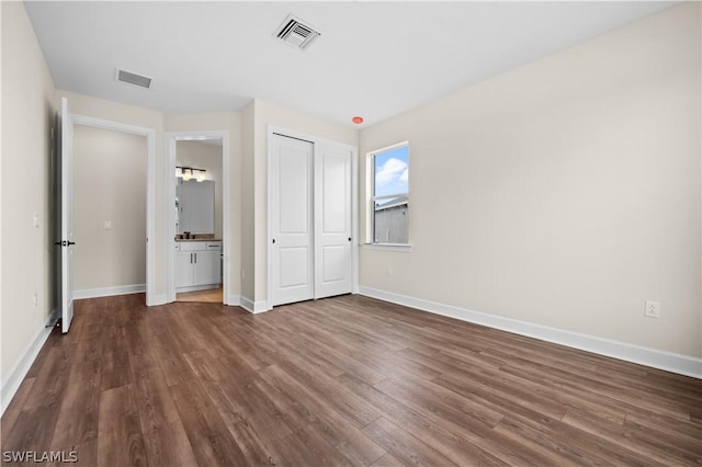 unfurnished bedroom with ensuite bathroom and dark hardwood / wood-style flooring