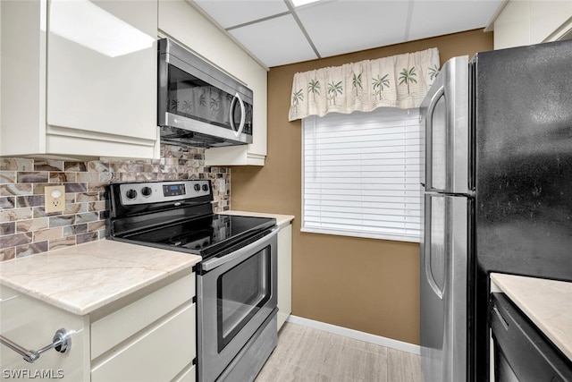 kitchen with stainless steel appliances, a paneled ceiling, tasteful backsplash, and light hardwood / wood-style flooring